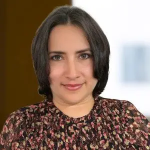 Woman with short, dark hair and light eyes, wearing a floral patterned top, poses in front of a softly blurred indoor background. No focus keyphrase set.